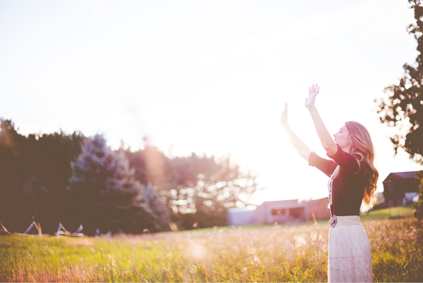 Woman with arms raised in a field with trees and sunlight